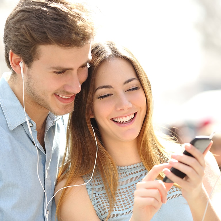 pareja compartiendo audifonos y observando la pantalla de un smartphone 768 x 768 pixeles 